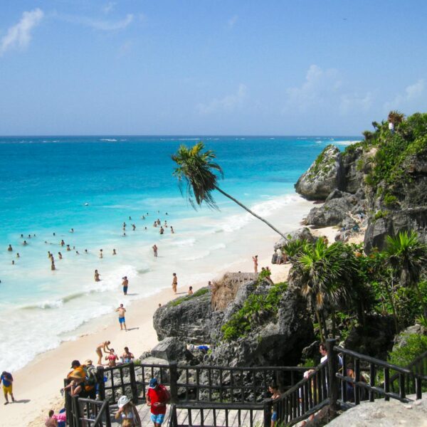 Crowded beach with turquoise water and rocky cliffs under a bright sky.